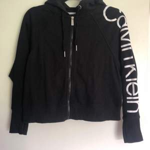 Svart croppad hoodie med dragkedja från Calvin Klein med vitt tryck på ärmen. Strl xs i bra skick. Köparen står för frakten! 🌸