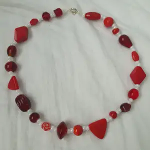 Rött halsband med blandade pärlor. Går att knäppa. Längd: 40cm