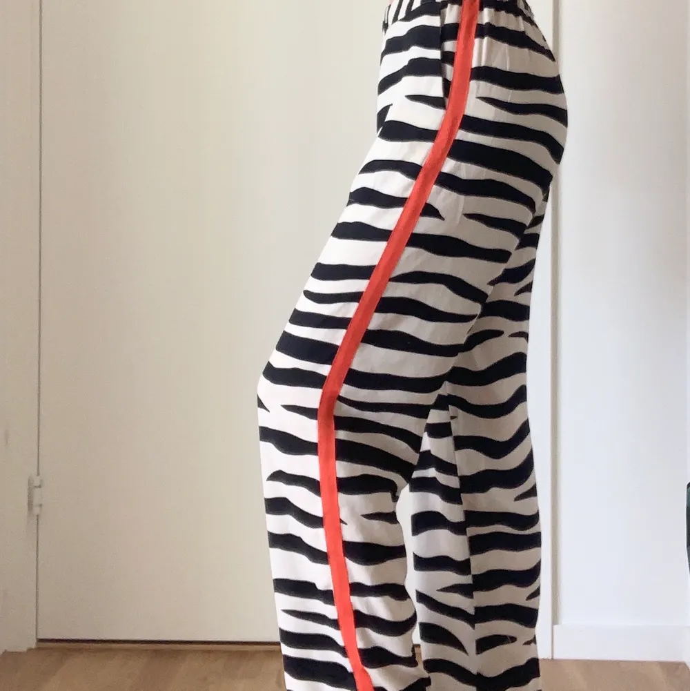 Slutsålda byxor från Lindex. Byxorna är i zebra tyg med en orange/röd detalj längs båda sidorna. Storlek XS. Jag är 162 lång och byxorna passar mig perfekt i längden. . Jeans & Byxor.
