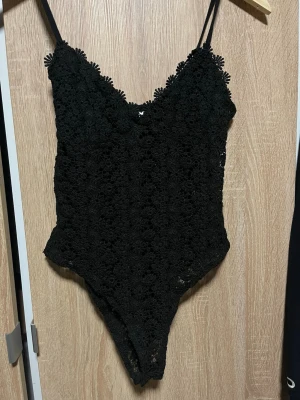 Svart spetsbody från H&M - Säljer en svart body från H&M i storlek S. Bodyn är gjord i blommig spets med tunna axelband och v-ringad hals. Materialet är genombrutet och ger en elegant look. Perfekt för dig som gillar detaljer och en feminin stil. Säljer då den aldrig har kommit till användning men den är super fin 
