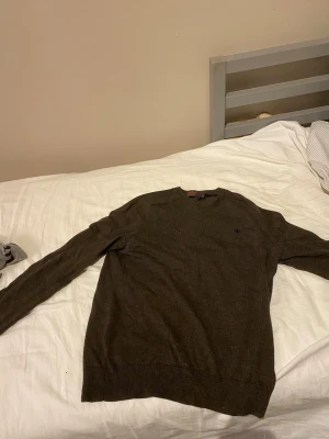 Mörkbrun stickad Morris tröja med rund hals - Mörkbrun stickad tröja med rund hals och långa ärmar. Tröjan har ribbade muddar vid ärmslut och nederkant samt en liten broderad logga på bröstet. Perfekt för lager på lager. Äkta Morris! Säljs för den är för liten