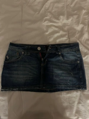 Mörkblå jeanskjol  - Säljer en mörkblå jeanskjol med klassisk femficksdesign, bälteshällor och snygga kontrastsömmar. Kjolen har en kort och lågmidjad passform och detaljerade bakfickor med broderade mönster. Perfekt för dig som gillar denim och vill ha en enkel men trendig look. Det står ingen storlek men midjemåttet är ca 35-36cm 