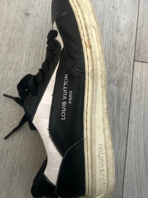 Louis Vuitton svartvita sneakers - Louis Vuitton sneakers i svart och vitt med tydlig logga på sidan och sula. Skon har svarta läderdetaljer, vita meshpaneler och svart snörning. Tjock vit sula med präglad logotyp. Klassisk låg modell med exklusiv känsla.