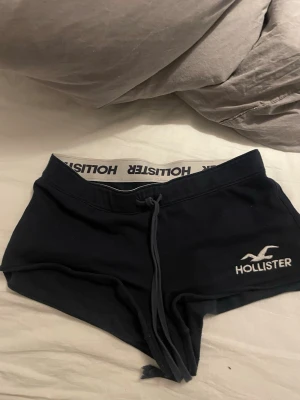 Svarta shorts från Hollister med snörning - Säljer ett par svarta shorts från Hollister med bred resår i midjan där Hollister-loggan syns tydligt. Shortsen har snörning framtill och är tillverkade i mjukt material, perfekta för avslappnade dagar.