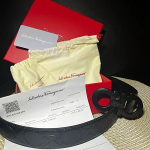 Bälte ifrån Salvatore Ferragamo 105cm - Snyggt svart bälte från Salvatore Ferragamo med ikoniskt dubbel-Gancio-spänne i matt svart metall. Bältet har präglat mönster längs hela remmen och levereras med originalförpackning och dustbag. Perfekt accessoar för att lyfta din outfit.