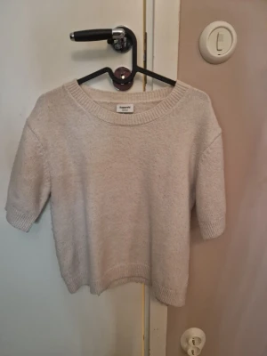 Beige stickad tröja från Kappahl - Mysig beige stickad tröja från Kappahl med rund halsringning och halvlånga ärmar. Tröjan har ribbade muddar vid ärmslut och nederkant, och är gjord i ett mjukt material som passar perfekt till lager på lager. Är lite knottrig