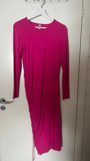 Rosa långärmad klänning från JDY - Säljer en snygg rosa långklänning från JDY med långa ärmar och rund halsringning. Klänningen har en tight passform och cool snörningsdetalj på sidan som ger extra edge. Perfekt för dig som vill sticka ut med färg och stil.
