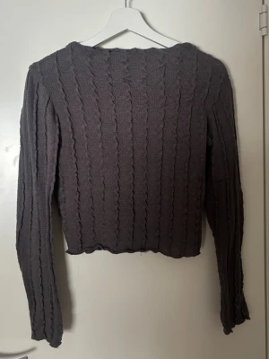 Grå kabelstickad tröja Gina Tricot - Mysig grå kabelstickad tröja från Gina Tricot med lång ärm och rund hals. Tröjan har ett vågigt stickat mönster och är lätt croppad i modellen. Perfekt för lager på lager och enkel att matcha med jeans eller kjol.