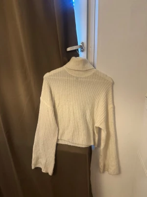Vit stickad tröja - Säljer en vit ribbstickad polotröja med croppad passform och långa ärmar. Tröjan har en hög polokrage och är gjord i ett mjukt, stretchigt material. Perfekt för lager på lager och enkel att styla till olika outfits. Lite nopprig