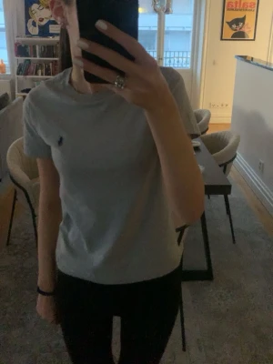 Ljusgrå t-shirt från Ralph Lauren - Säljer en ljusgrå t-shirt från Ralph Lauren med den klassiska lilla broderade loggan på bröstet. T-shirten har korta ärmar och en normal passform. Perfekt basplagg till garderoben.