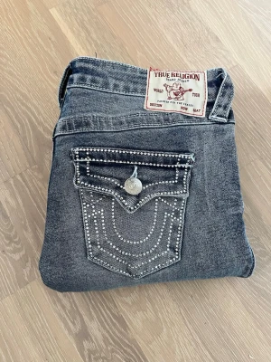 True Religion Joey Low Rise Flare Jeans - Säljer ett par blå Joey Low Rise Flare jeans från True Religion. De har låg midja, utsvängda ben och klassiska detaljer med silverfärgade knappar och fickor fram. Endast använda en gång då de var fel storlek