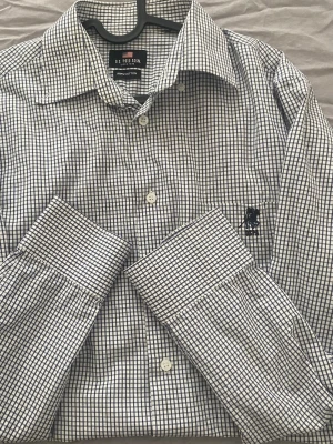 Rutig skjorta från U.S. Polo Assn. - Klassisk långärmad skjorta från U.S. Polo Assn. i vitt och mörkblått rutmönster. Skjortan har knappar framtill, bred krage och broderad logga på bröstet. Tillverkad i 100% bomull för en skön och luftig känsla.