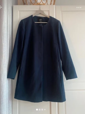 Mörkblå kappa Lindex - Stilren mörkblå kappa från Lindex med en diskret knäppning framtill. Kappan har rundad halsringning och långa ärmar. Tillverkad i ett mjukt tyg som ger en elegant look. Perfekt för dig som gillar enkel och klassisk stil. 84 cm lång.