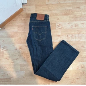 Levi's 501 mörkblå jeans W30 L32 - Klassiska Levi's 501 jeans i mörkblå denim. Rak passform med fem fickor och ikonisk läderpatch bak i midjan. Perfekta för dig som gillar tidlös stil och vill ha ett par jeans som funkar till allt. Jeansmaterialet är slitstarkt och håller länge.