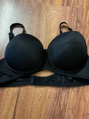 Svart push-up bh med bygel - Snygg svart push-up bh med bygel och vadderade kupor. Justerbara axelband och hakknäppning bak. Enkel och stilren design som passar till det mesta. Materialet känns mjukt och bekvämt mot huden.