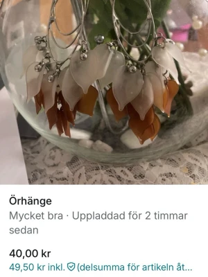 Blommiga örhängen i brunt och vitt - Unika örhängen med hängande blommor i plast i nyanser av vitt, beige och brunt. Örhängena har silverfärgade detaljer och en organisk, bohemisk känsla. Perfekta för dig som vill sticka ut med ett kreativt smycke.
