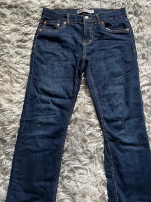 Mörkblå  jeans från Levi's - Säljer ett par klassiska mörkblå jeans från Levi's med raka ben och fem fickor. Jeansen har kontrastsömmar och den ikoniska Levi's-lappen bak i midjan. Perfekta till vardags och gjorda i slitstarkt denimtyg.