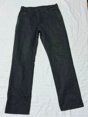 Wrangler Texas Stretch svarta jeans - Säljer ett par svarta Wrangler Texas Stretch jeans med rak passform. Jeansen har klassisk femficksdesign och är tillverkade i stretchigt denimtyg för extra komfort. Perfekta för dig som gillar en enkel och tidlös look.