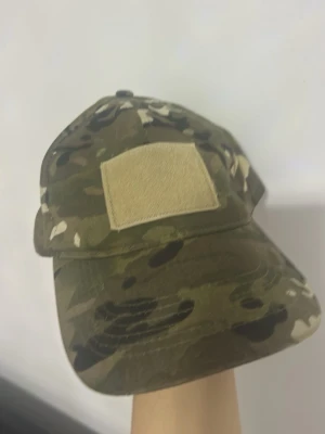 Keps med camomönster och patch (militär mönster) - Cool keps med militärinspirerat camomönster i gröna och bruna nyanser. Framtill finns en beige patch för att fästa märken eller badges. Kepsen har böjd skärm och justerbar baksida. Perfekt för dig som gillar streetstyle eller outdoor-vibes. Den är köpt från stadium! Original priset för kepsen är 350kr 