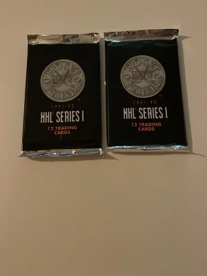 NHL Pro Set Platinum 1991-92 kort - Två oöppnade paket NHL Pro Set Platinum Series I från säsongen 1991-92. Varje paket innehåller 12 samlarkort. Svart och silverfärgad förpackning med tydlig NHL-logga. Perfekt för hockeyfans och samlare av sportkort.