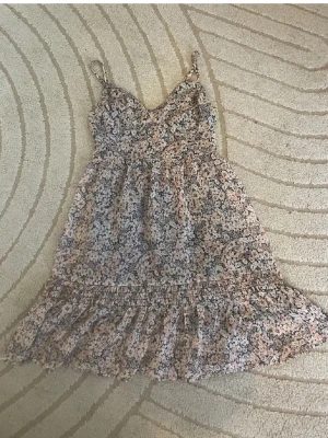 Hollister mesh volangklänning❤️ - Söt kortklänning med smala axelband och volang nertill. Klänningen har ett blommigt mönster i beige, svart och vit med inslag av ljusa toner. Perfekt för varma dagar och har en luftig passform.