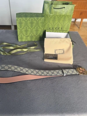 Gucci bälte - Snyggt Gucci GG  bälte med klassiskt monogrammönster i beige och grått. Bältet har ett stort guldigt GG-spänne och insida i ljusrosa skinn. Kommer med originalförpackning, dustbag och band. Oanvänd.     110cm.                                      Skriv vid frågor!!!!