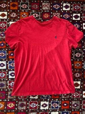 Vintage Ralph Lauren - Röd t-shirt från Ralph Lauren med klassisk passform och liten blå logga broderad på bröstet. T-shirten har rund halsringning och är tillverkad i mjuk bomull. Perfekt för en avslappnad och stilren look. Hör av dig vid frågor om T-shirten! 