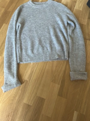 beige  ribbstickad tröja - En enkel och stilren ljusgrå ribbstickad tröja med rund hals och långa ärmar. Tröjan har en rak passform och uppvikta ärmslut, perfekt för en avslappnad look. Materialet känns mjukt och bekvämt mot huden.