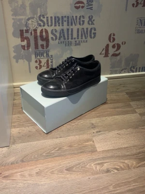 Lanvins  - Stilrena svarta sneakers i mocka med lågt skaft och svarta skosnören. Klassisk design med rund tå och diskreta sömmar. Passar perfekt till jeans eller chinos för en clean look.