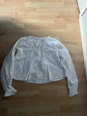 Vit blus prickig - Söt vit blus från Gina Tricot med långärmade ärmar och volang nedtill. Blusen har diskret prickig struktur i tyget och liten volangkant vid halsen. Perfekt att styla med jeans eller kjol för en trendig look.