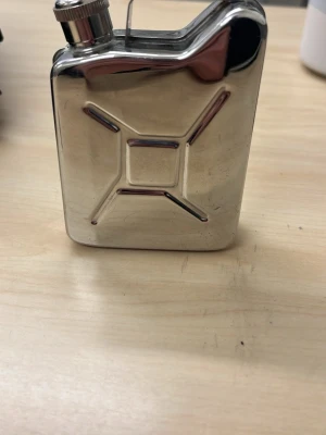 Plunta i form av bensindunk, silver - En liten plunta i blankt silverfärgat metallmaterial, designad som en klassisk bensindunk. Skruvkork och kompakt format, perfekt att ta med på äventyr eller som rolig present. Har bara haft vatten i den för att se så den inte läcker 