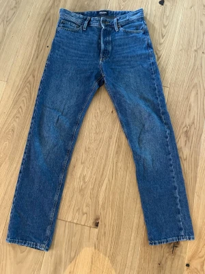 Blå relaxed jeans från Jack & Jones - Säljer ett par blå jeans från Jack & Jones, modell Relaxed/Chris. Jeansen har en avslappnad passform med raka ben och klassisk femficksdesign. Tillverkade i slitstark denim med kontrastsömmar. Perfekta för en chill och stilren look. Storlek 28/32 och i mycket fint skick