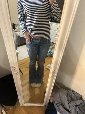 Blå slitna bootcut jeans - Säljer ett par blå bootcut jeans med slitningar och hål på knäna. 