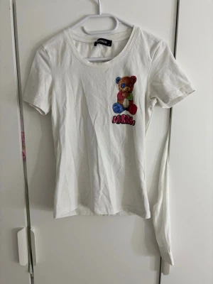 Vit t-shirt med nalle från Barrow - Vit t-shirt från Barrow med färgglad nalle-tryck både fram och bak samt textdetaljer. T-shirten har rund halsringning och korta ärmar. Perfekt för dig som gillar lekfulla och unika prints.
