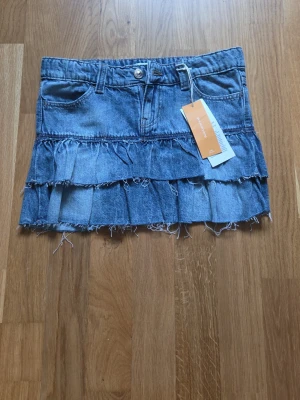 Blå, kort, lowwaist volangkjol i denim från gina tricot - Snygg blå jeanskjol från gina med volangdetaljer och råa kanter. Kjolen har bälteshällor och är tillverkad i klassisk denim. Perfekt för dig som gillar en trendig och avslappnad stil.