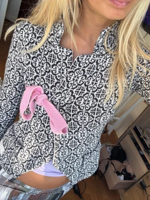 Odd Molly  mönstrad kofta med rosa rosett - Unik svartvit kofta med grafiskt mönster och en söt rosa rosett framtill. Koftan har figurnära passform, ståkrage och är tillverkad i ett stickat material. Perfekt för dig som vill sticka ut med en cool detalj.