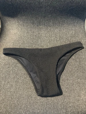 Svarta bikiniunderdel i ribbat tyg - Snygga svarta bikinitrosor med ribbad struktur och klassisk midja. Trosorna har en enkel och stilren design som passar perfekt till alla typer av bikiniöverdelar. Materialet är stretchigt och bekvämt för en skön känsla på stranden eller vid poolen.