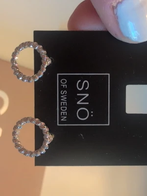 Silverfärgade örhängen från SNÖ of Sweden - Snygga örhängen i silverfärg. Dom är inte från Snö. De är runda och har en tvinnad design som ger en cool och modern look. Perfekta för att lyfta vilken outfit som helst. Stiftmodell för enkel användning. Dom är inte rostfria.