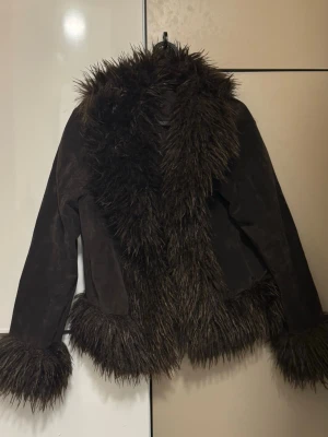 Brun pälsjacka med fuskpälsdetaljer - Säljer en brun pälsjacka med stora fluffiga fuskpälsdetaljer längs krage, ärmslut och nederkant. Jackan har en cool retrovibe och är gjord i mockaimitation med mjuk känsla från Gina Tricot.🤎🤍 ordinarie pris: 899kr