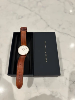 Daniel Wellington Klocka - Daniel Wellington Durham klocka med brunt läderband och ur i pläterat rosegulg. Mycket bra skick och allt original med. Skriv vid frågor.