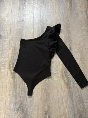 Svart body - En superfin svart body, enärmad med fin volang på den långärmade sidan. Perfekt till sommaren och annat. Köpt på New yorker för ca 3-4 år sedan, storlek S. Har bara haft på mig ca 3 gånger. Kontakta för fler frågor eller bilder🖤🖤