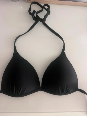 Svart trekantsbikinitopp XS - (Har ej använt!) Snygg svart bikinitopp i trekantsmodell med knytband i nacken. Tillverkad i 80% polyamid och 20% elastan för en stretchig och bekväm passform. Perfekt för strand eller poolhäng.