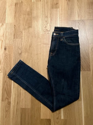 Blå Nudie Jeans  - Klassiska mörkblå Nudie Jeans för män. Byxorna är nyskick inga skador/slitage. Storlek Waist 27 / Lenght 30. Hör av dig vid intresse/frågor. PRIS KAN DISKUTERAS!