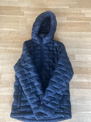 Svart lättviktsjacka med huva - Snygg svart lättviktsjacka med quiltat mönster och dragkedja framtill. Jackan har en praktisk avtagbar huva..