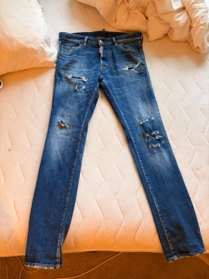Dsquared2 jeans - Säljer ett par blå jeans från Dsquared2 med skinny fit och slitna detaljer framtill. Jeansen har klassisk femficksdesign, knappgylf och patch med texten 'Eaten Heated' bak. Materialet är denim med stretch för skön passform.