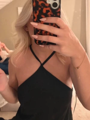 Svart halterneck linnetopp - Säljer en svart linnetopp med halterneck och smala axelband som korsas framtill. Toppen är ärmlös och har en clean, stilren look som passar perfekt till jeans eller kjol. Materialet känns mjukt och följsamt mot huden.