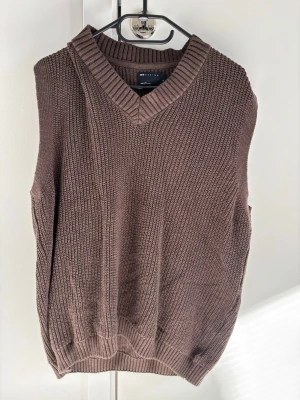 Brun stickad väst från ASOS DESIGN - Snygg brun stickad väst från ASOS DESIGN med v-ringad hals och bred ribbad kant. Perfekt att bära över en skjorta eller t-shirt för en trendig lager-på-lager-look. Tillverkad i mjukt material som känns bekvämt hela dagen.