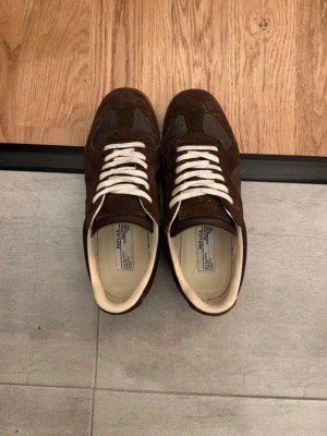 Margiela GAT - Snygga bruna sneakers från Maison Margiela i en mix av mocka och läder. Skorna har beige innersula och klassisk sula. Perfekt för dig som gillar stilrena och tidlösa sneakers med en lyxig touch.