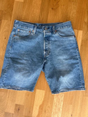 Levi's Premium blå jeansshorts - Klassiska blå jeansshorts från Levi's Premium med fem fickor och knappgylf. Modellen har en rak passform och är tillverkad i slitstark bomull. Perfekta för en avslappnad stil under varmare dagar.