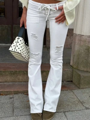 Vita bootcut jeans med snörning - Säljer ett par vita bootcut jeans från Gina Tricot Young 14+ med snörning i midjan och slitna detaljer på låren. Jeansen har låg midja och bootcut ben. Säljer då de var för små för mig 